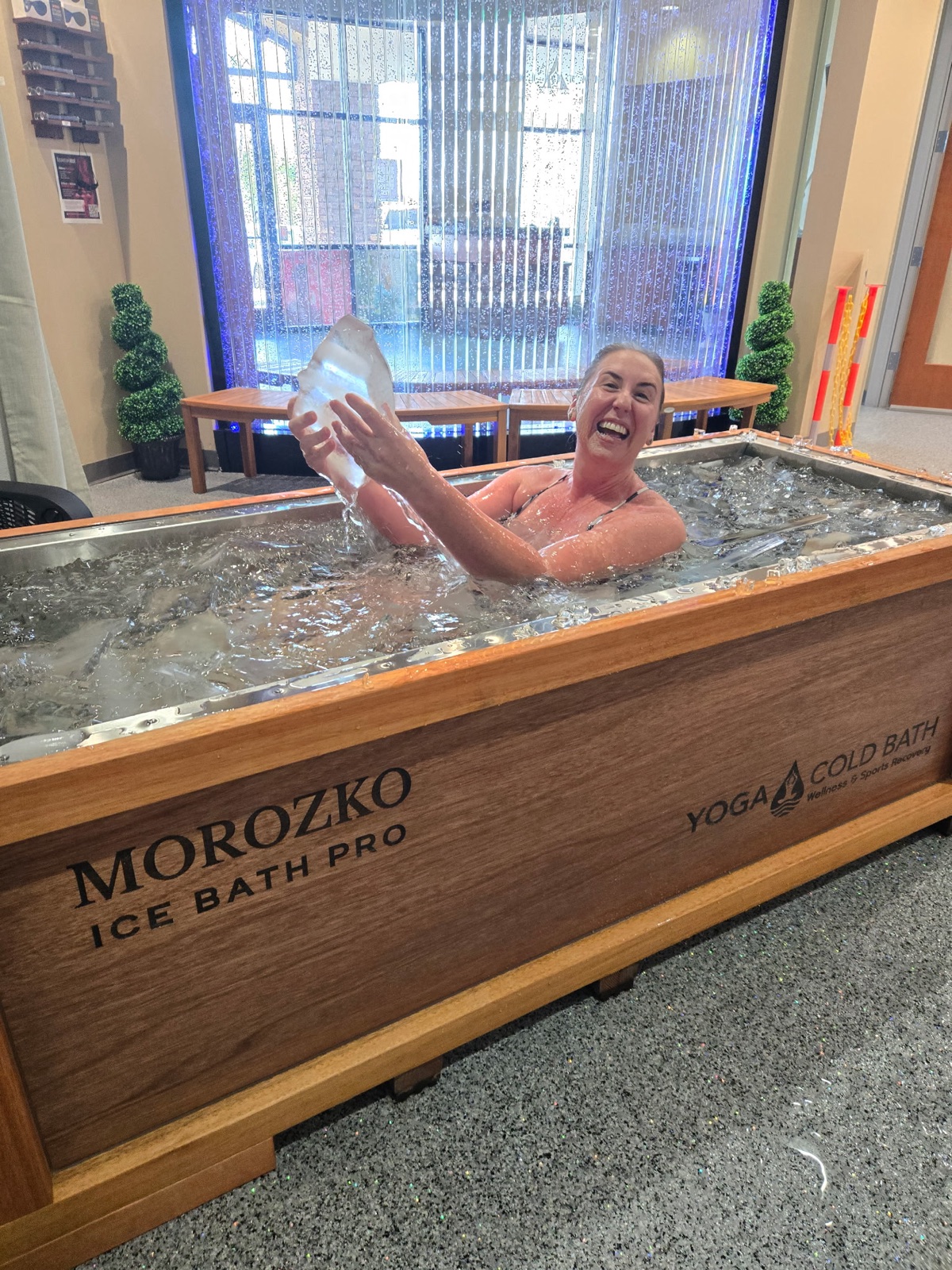 Member smiling and lifting a slab of real ice in the Morozko Ice Bath Pro at Yoga Cold Bath