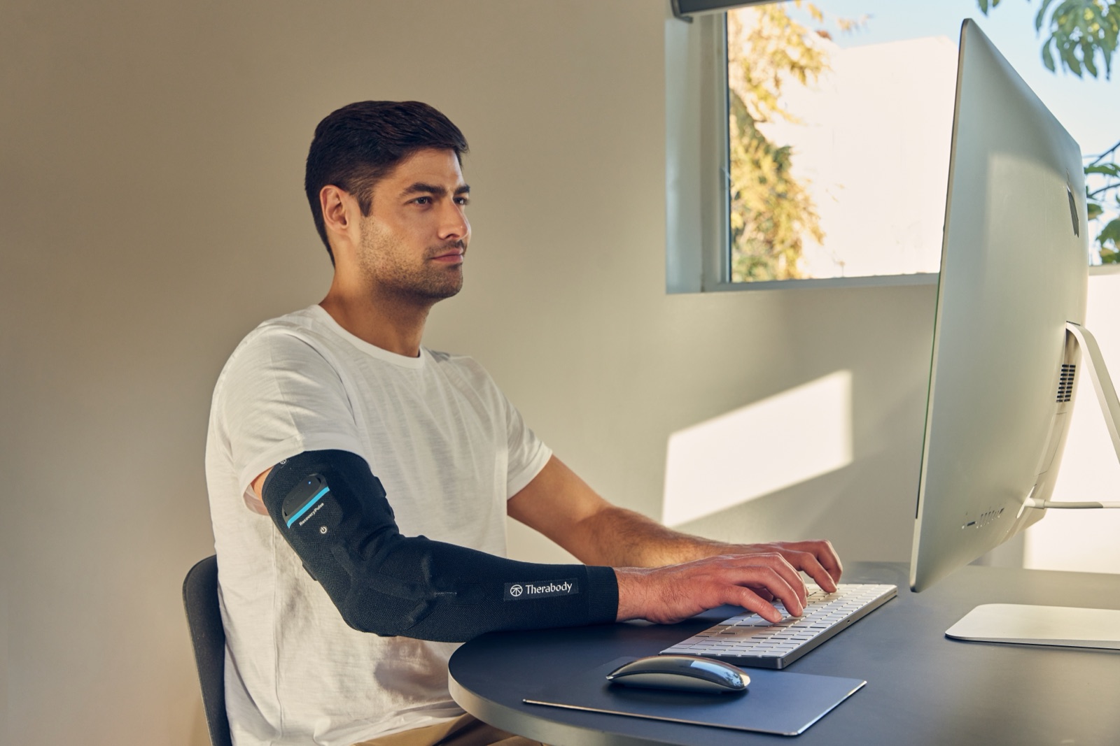 Person at a desk wearing the Therabody RecoveryPulse Arm compression sleeve