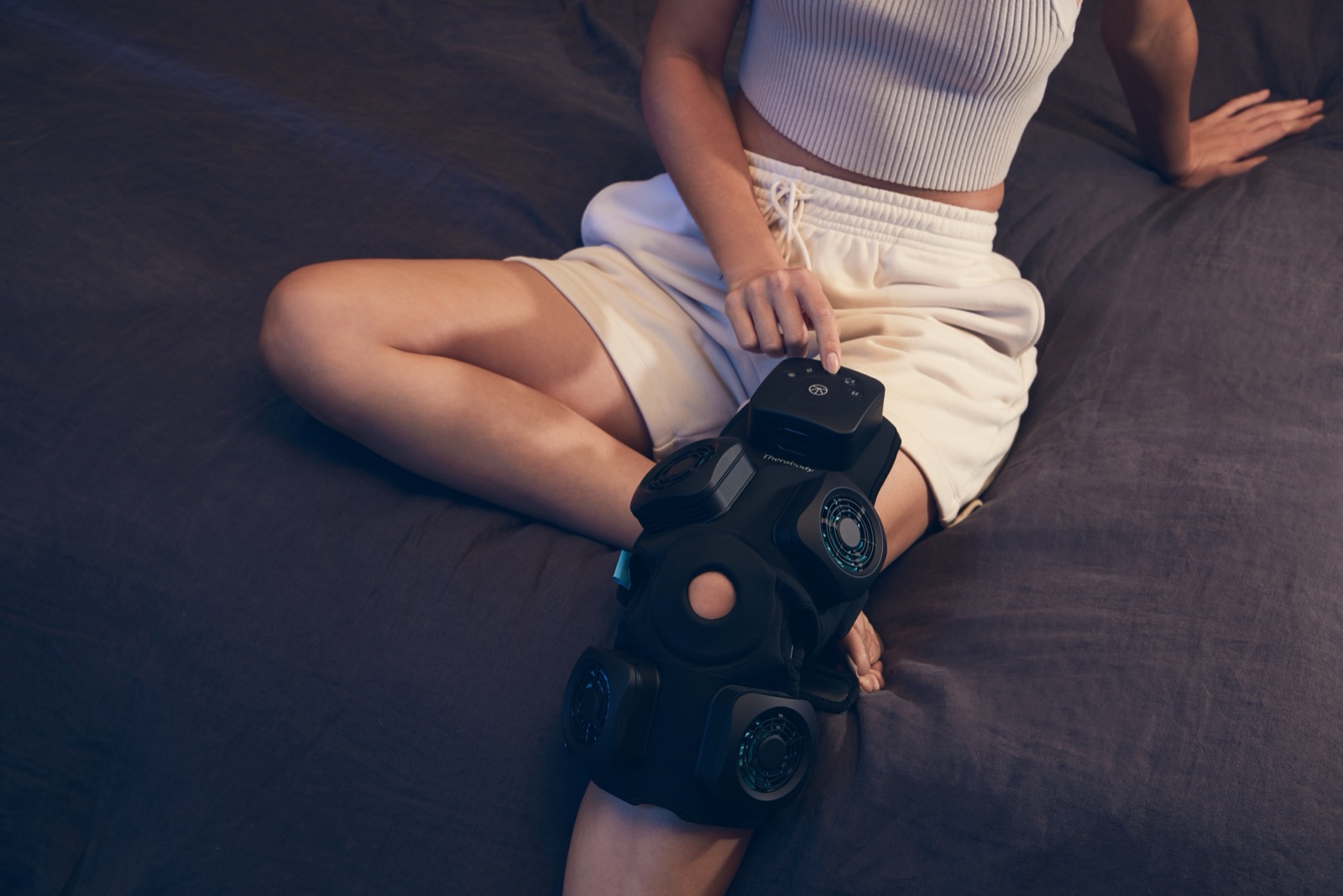 Person on a bed wearing the Therabody RecoveryTherm Knee wrap with cold, heat, and vibration therapy