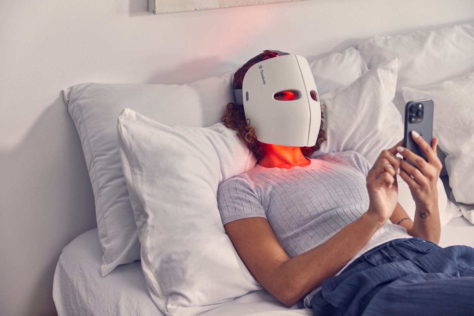 Person relaxing on a bed wearing the Therabody TheraFace Mask Glow LED light therapy mask