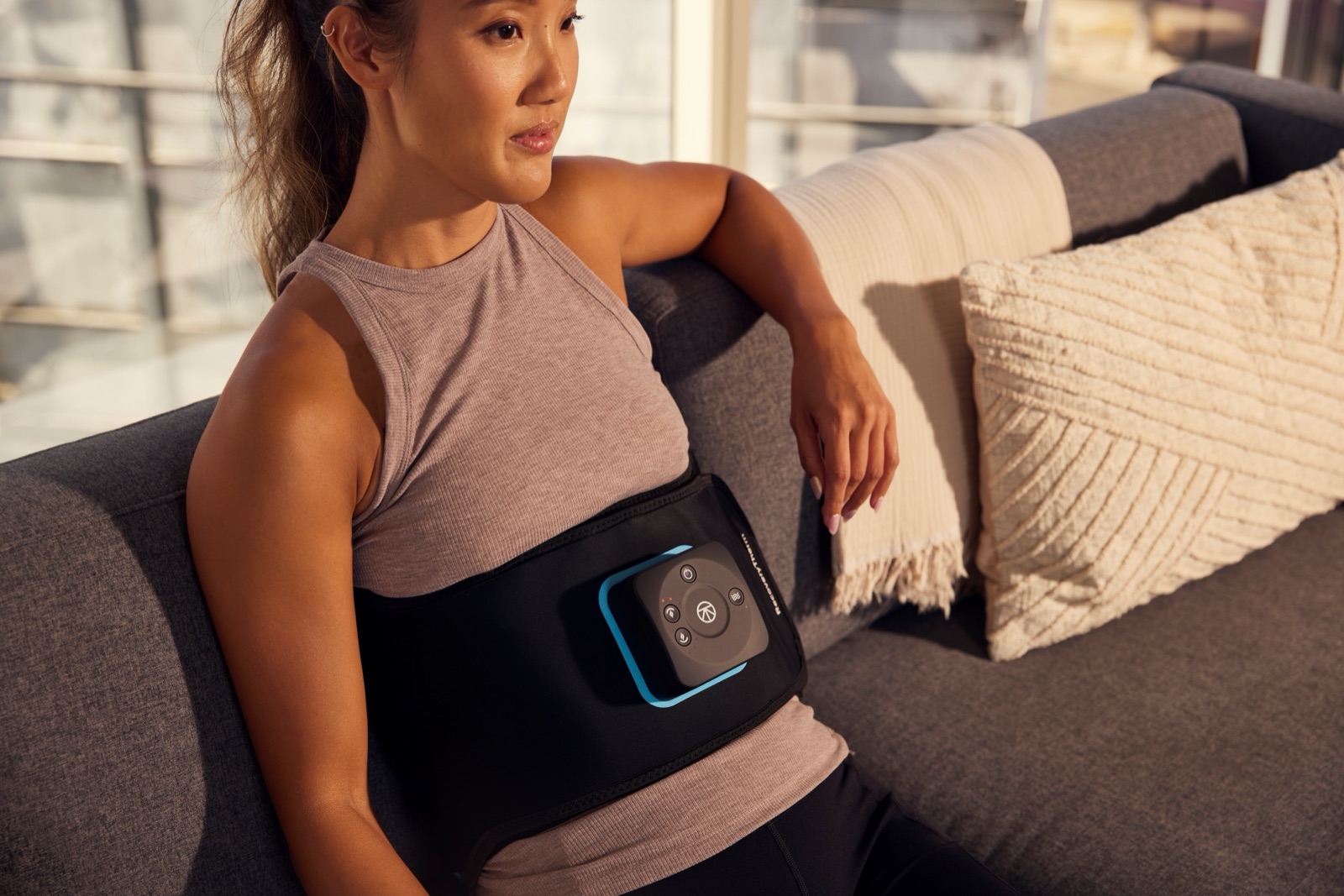 Person on a couch wearing the Therabody ThermBack LED back wrap